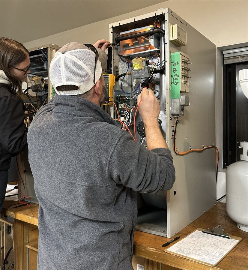 HVAC student wiring and testing an open gas furnace panel